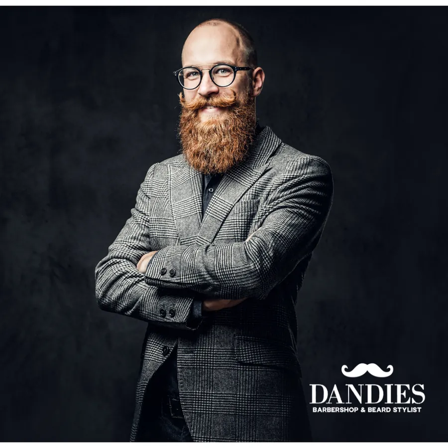 Bearded man with round glasses in a tweed jacket against a dark backdrop