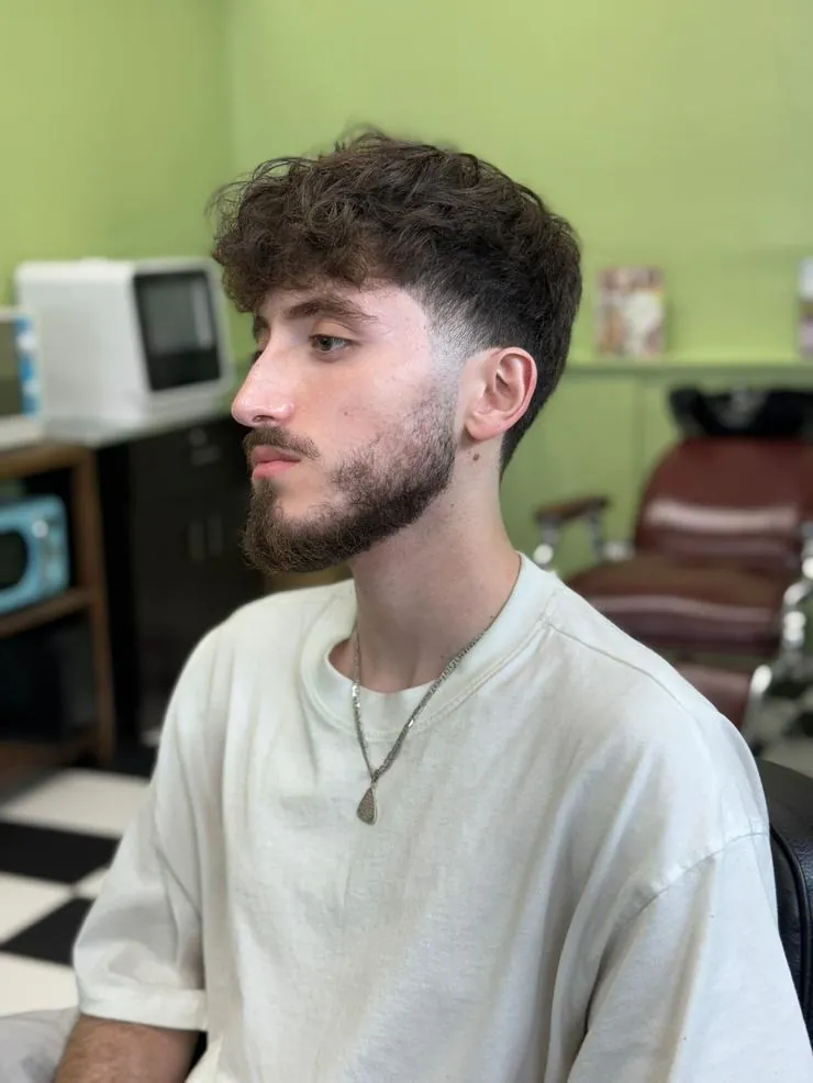 Young man with a curly textured top and low fade seated in the barbershop