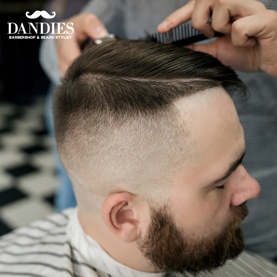Close-up of a skin fade with a combed-over top and trimmed beard as a barber works